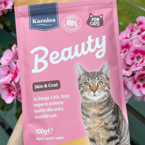 Hand holding Karnlea Beauty skin and coat topper for cats in pink pouch packaging